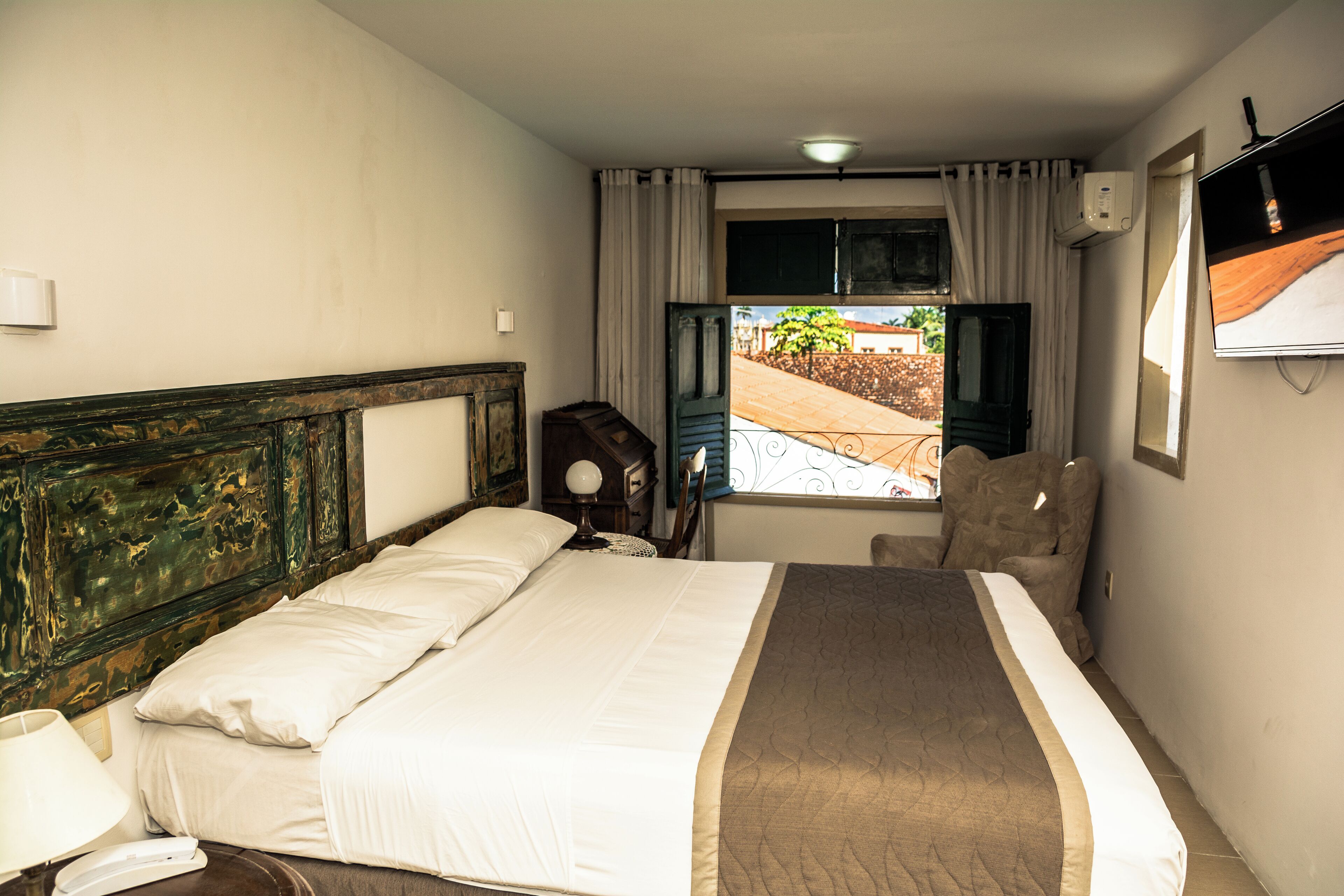 A hotel room with a large bed, a chair, a TV, and a window with curtains.