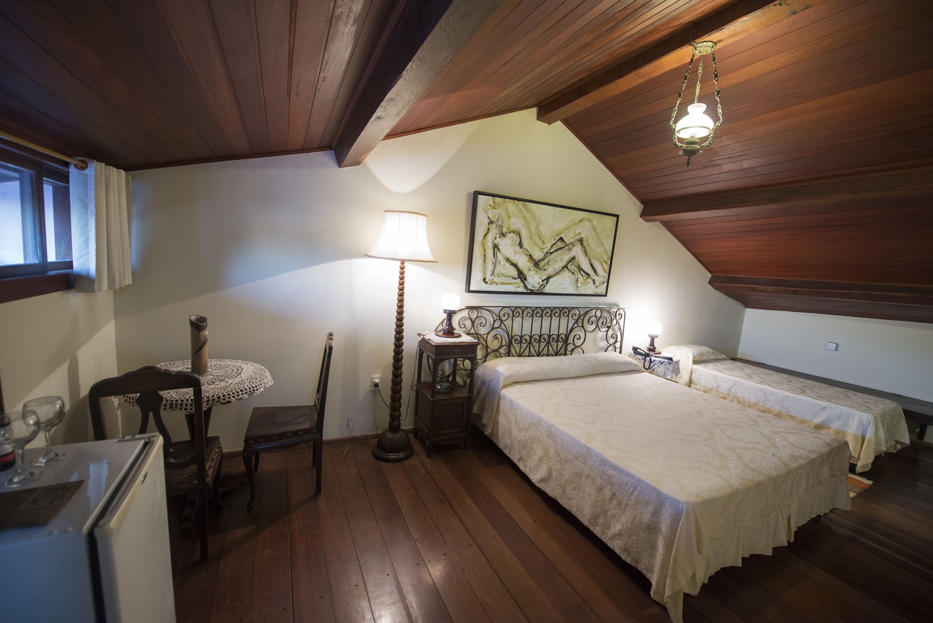 Un dormitorio acogedor con pisos de madera, una cama, una mesita de noche, una lámpara y un cuadro en la pared.