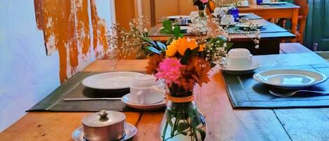 Una mesa de comedor dispuesta con platos, tazas y un jarrón de flores.