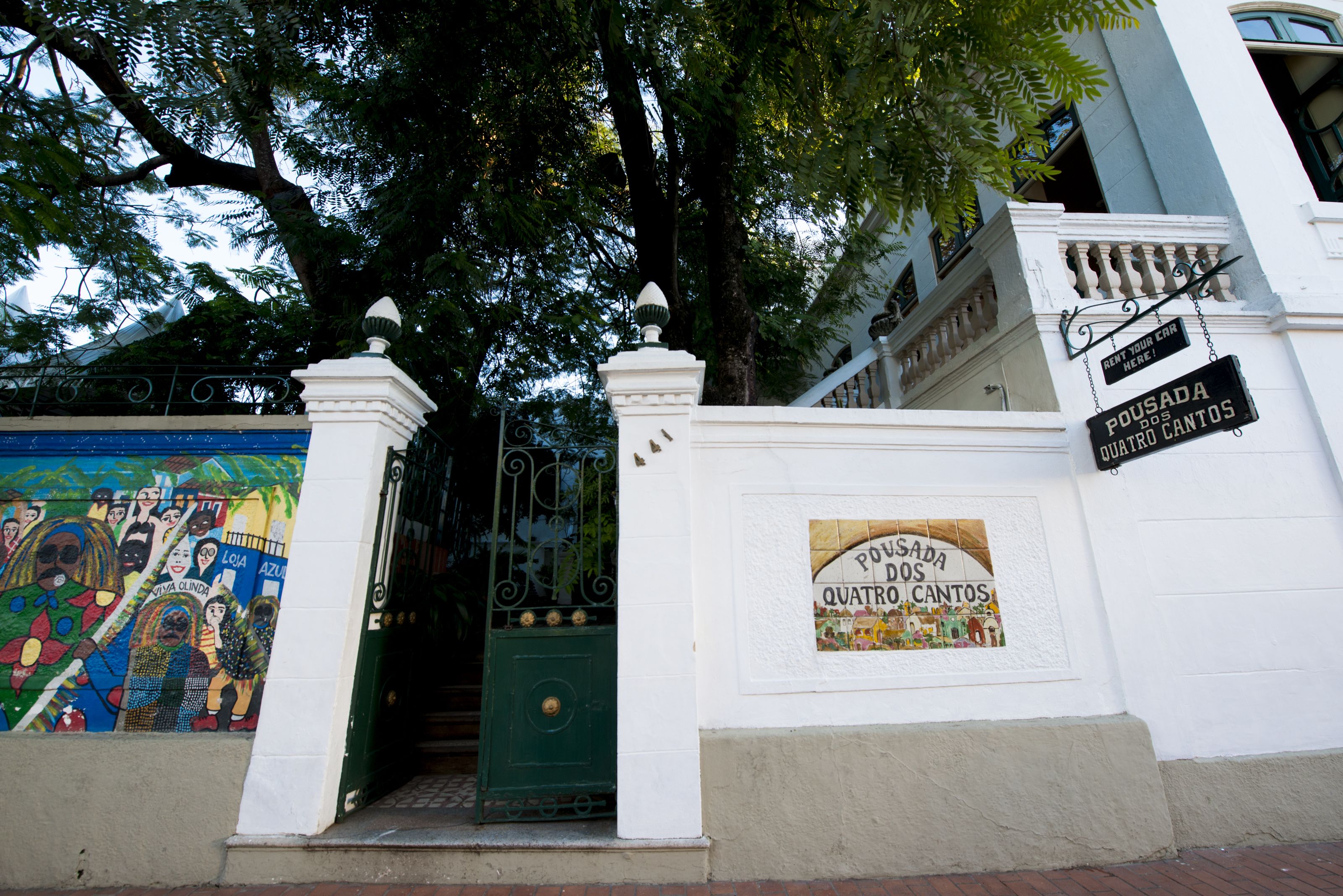 A building entrance with a green door, a mural on the left, and a sign reading "Pousada dos Quatro Cantos".