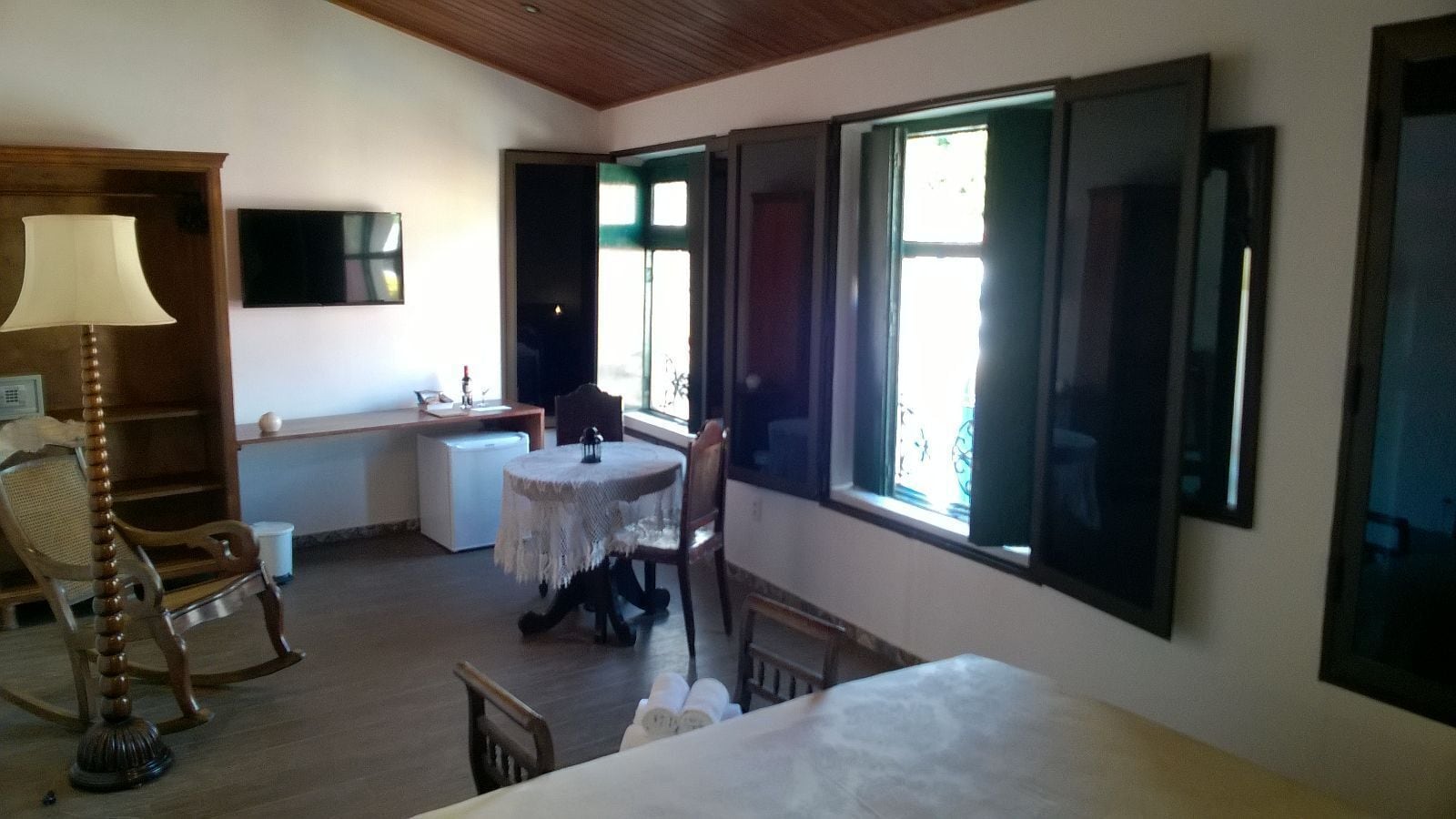 Una stanza con un letto, una scrivania, una sedia, una poltrona a dondolo, una lampada e ampie finestre.