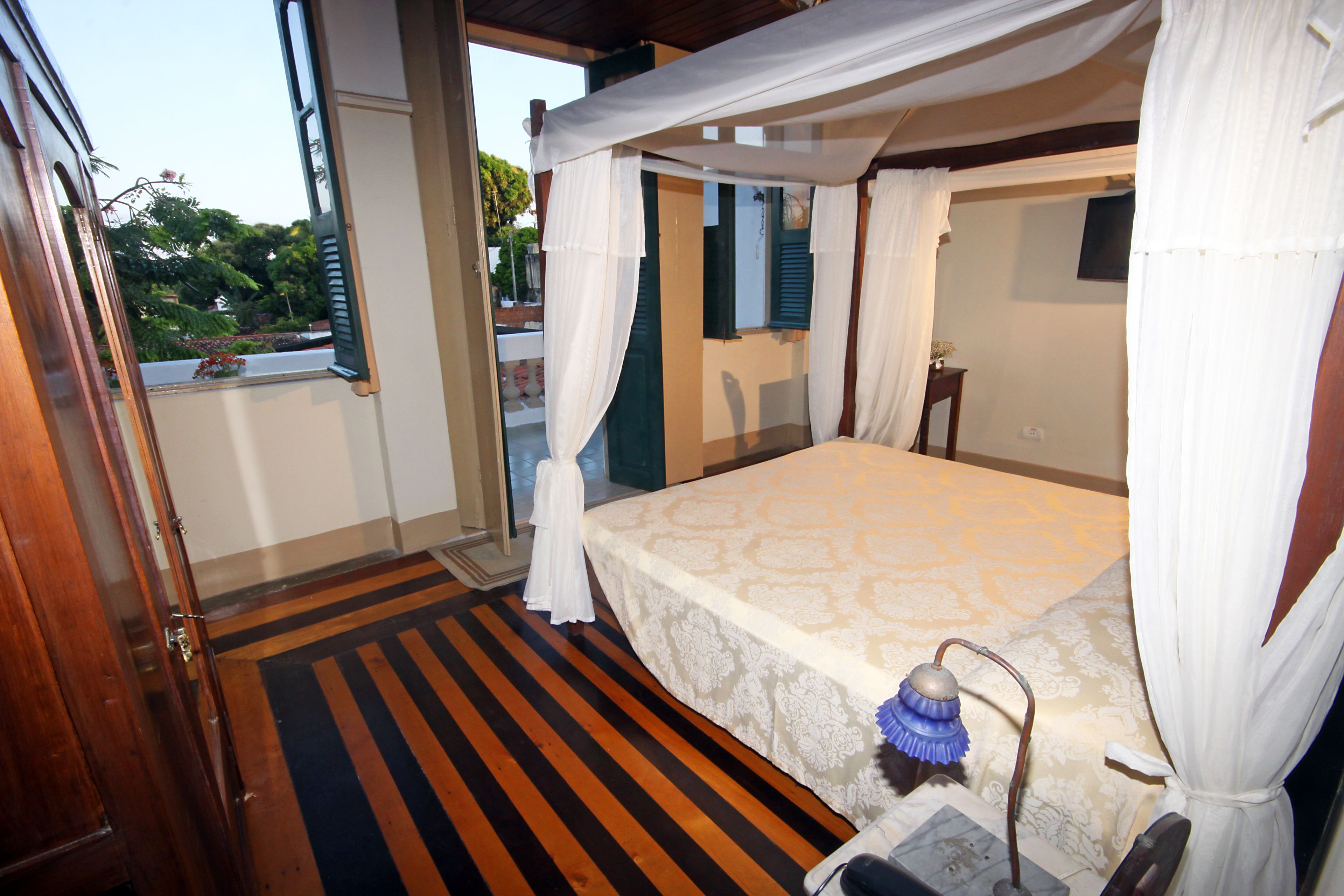 Un dormitorio con cama, mesita de noche, lámpara y ventana con cortinas.