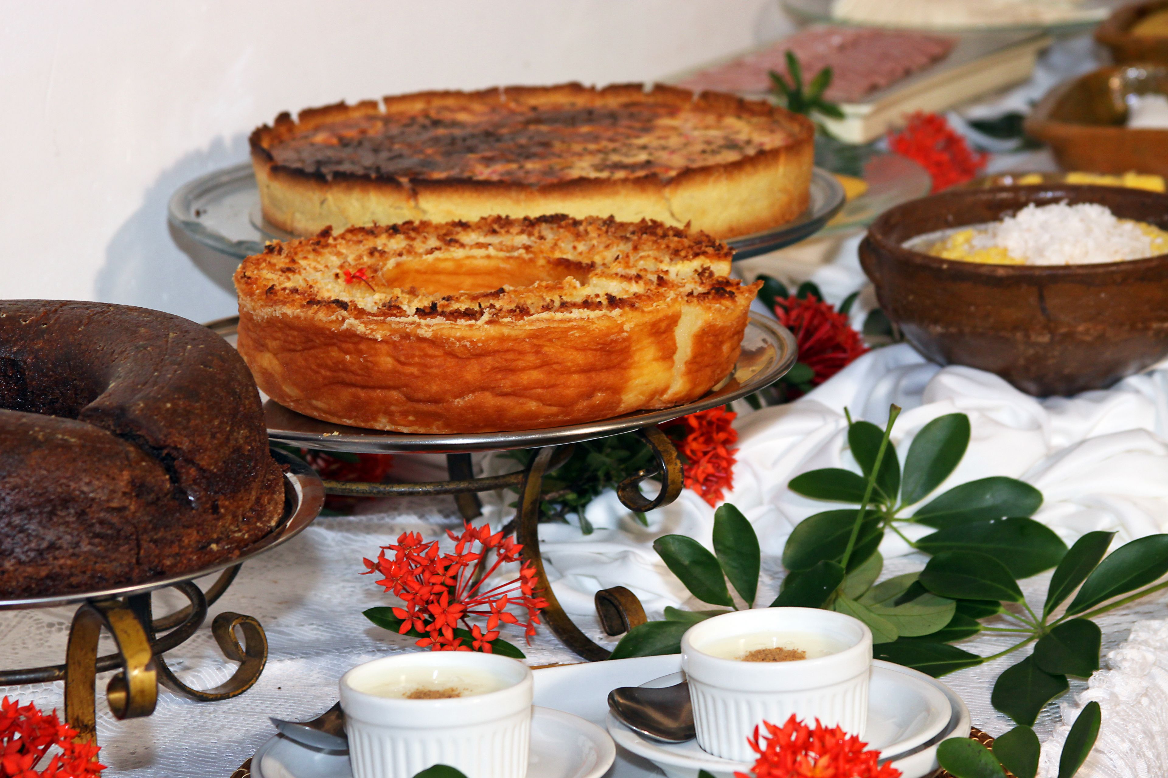 A dessert table with cakes and bowls of food, surrounded by decorative flowers.