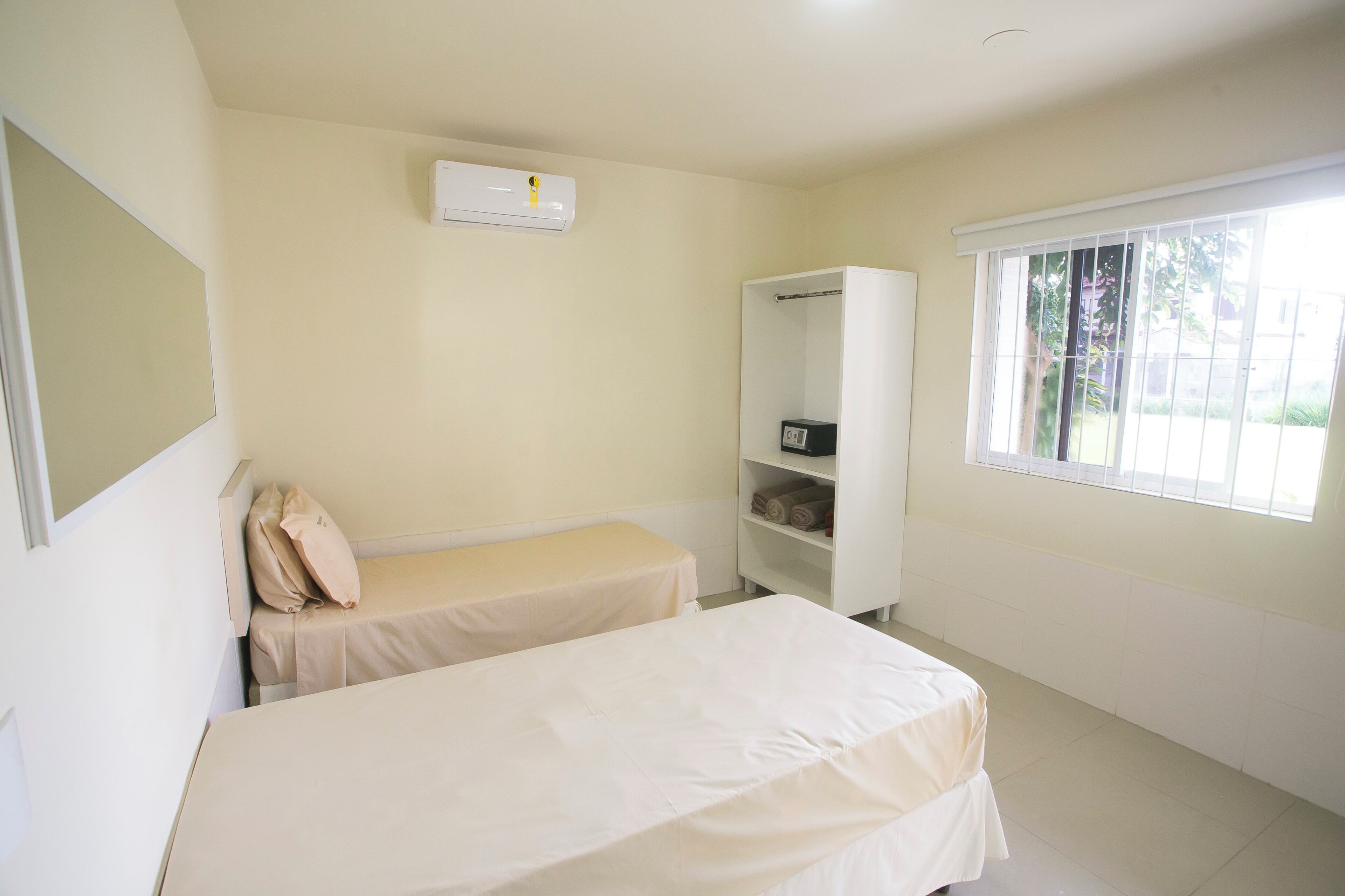 A room with two beds, a wardrobe, a window, and an air conditioning unit.