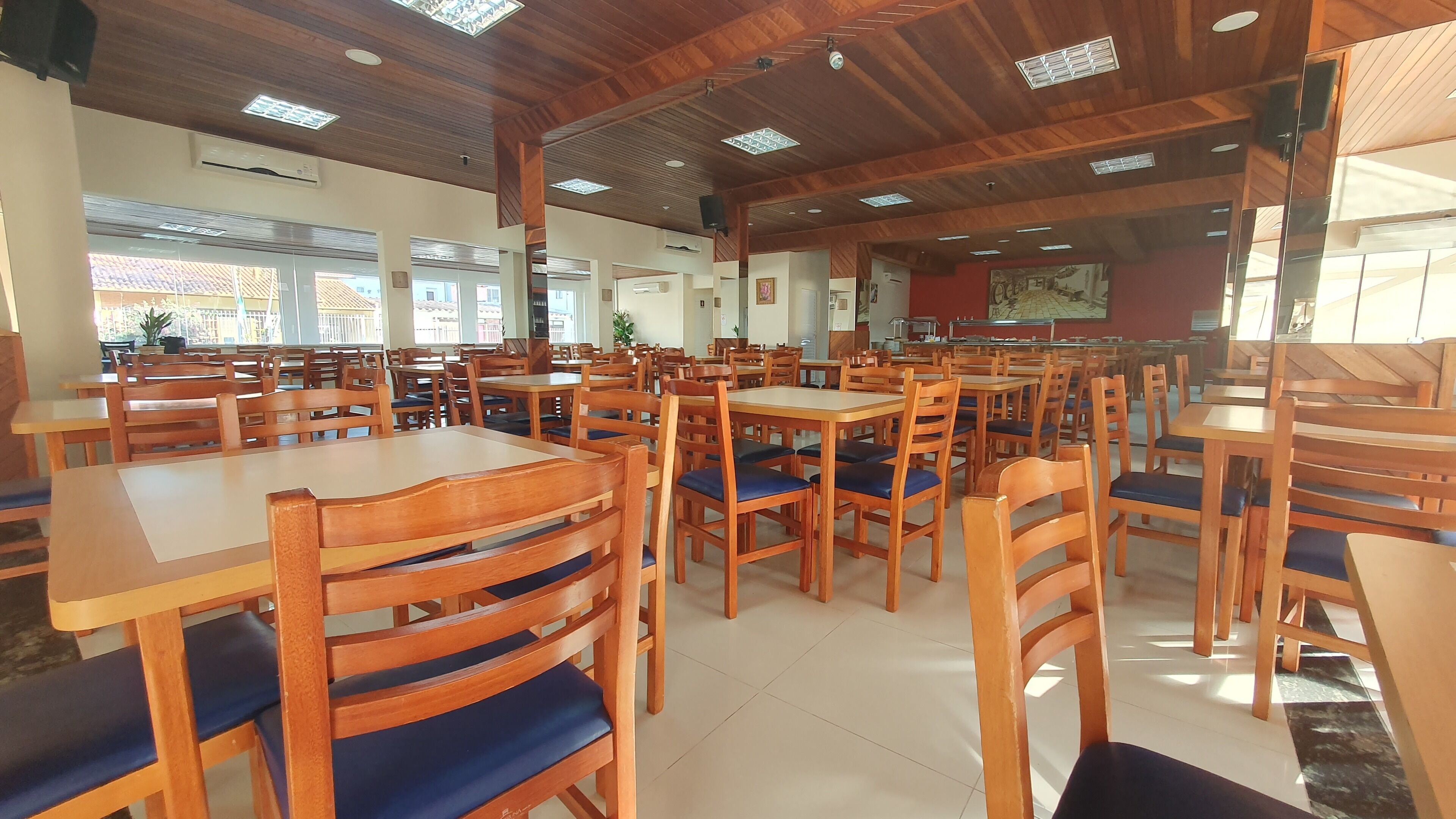 Un vaste espace dédié à la salle à manger, avec des tables et des chaises en bois, de grandes fenêtres et un plafond haut orné de poutres en bois.