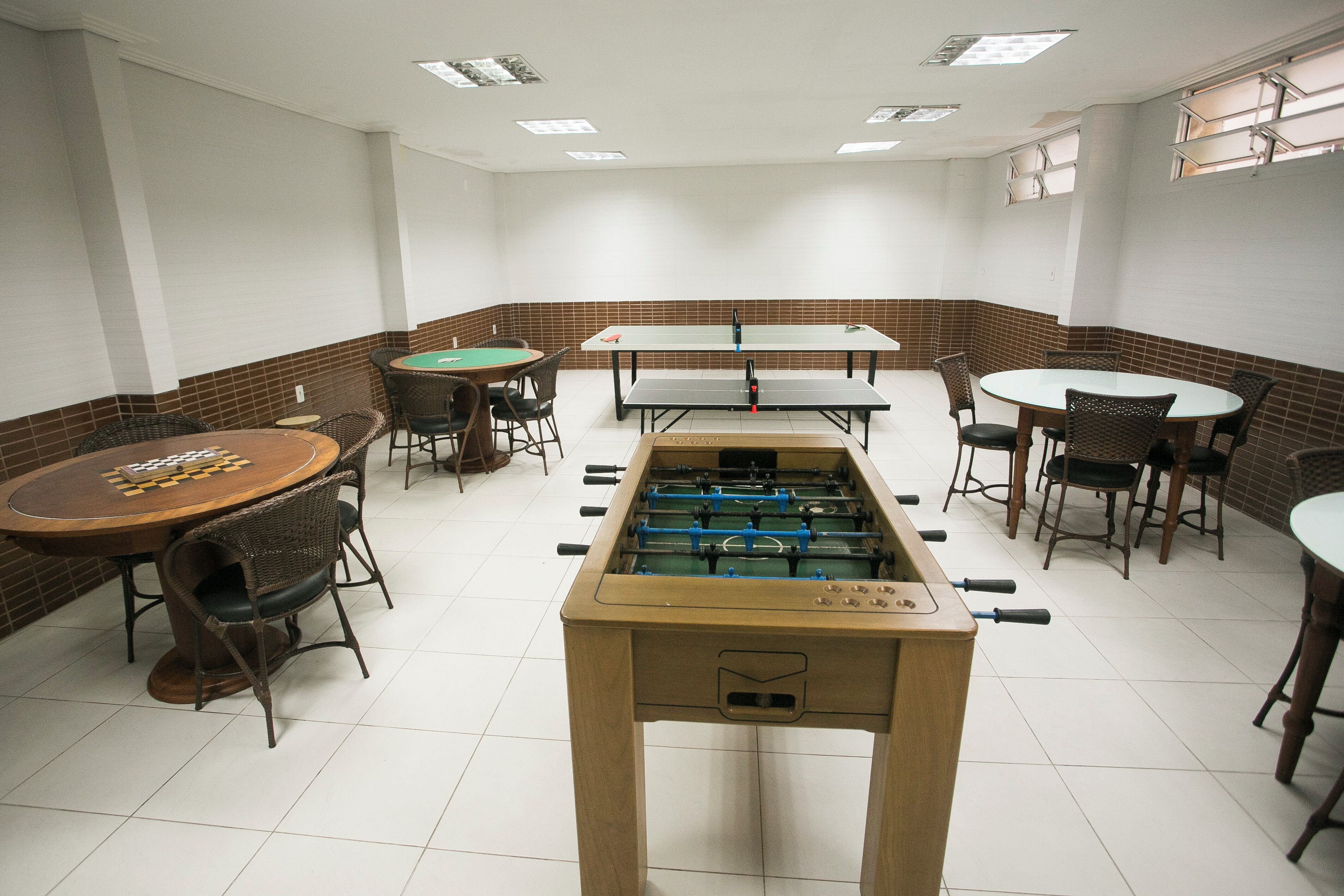A room with a foosball table, several tables with chairs, and a billiards table.