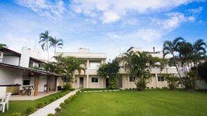A residential building with a well-maintained lawn, palm trees, and a clear sky. - THE - Tropicanas Hotel e Eventos (Florianópolis)