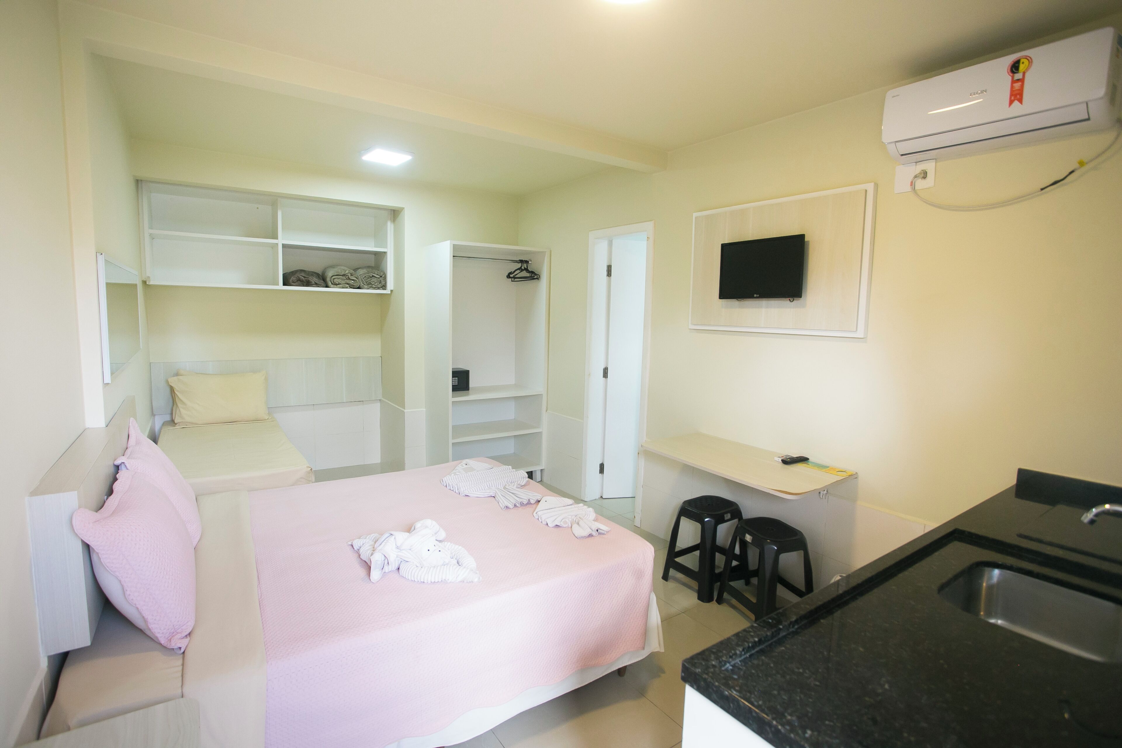 Una habitación de hotel con cama, escritorio, silla, televisión y kitchenette.