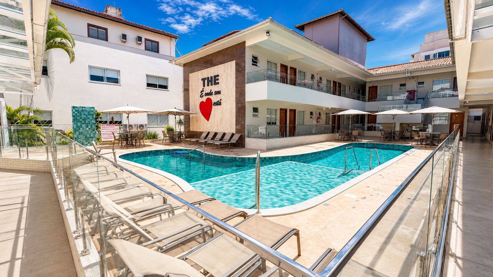 Un hotel con piscina, mobiliario exterior y un cartel con un símbolo de corazón.
