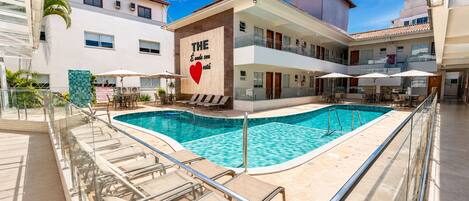 Un hotel con piscina, mobiliario exterior y un cartel con un símbolo de corazón.