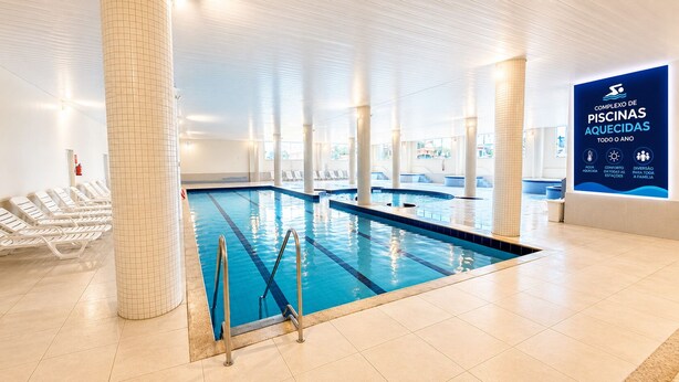 An indoor swimming pool with clear water, tiled walls, and lounge chairs. - THE - Tropicanas Hotel e Eventos (Florianópolis)