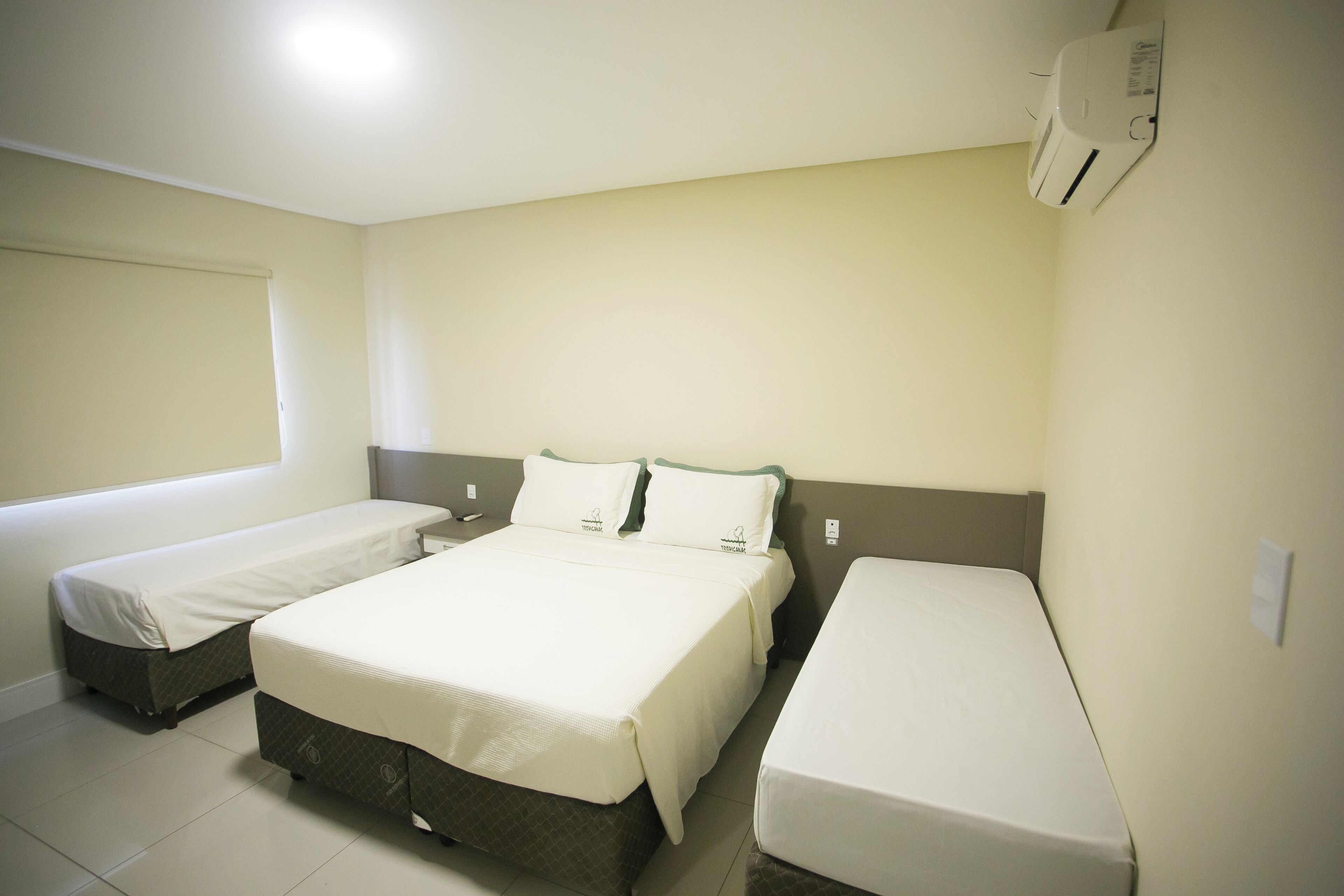 A hotel room with two single beds, a larger bed, and a window.