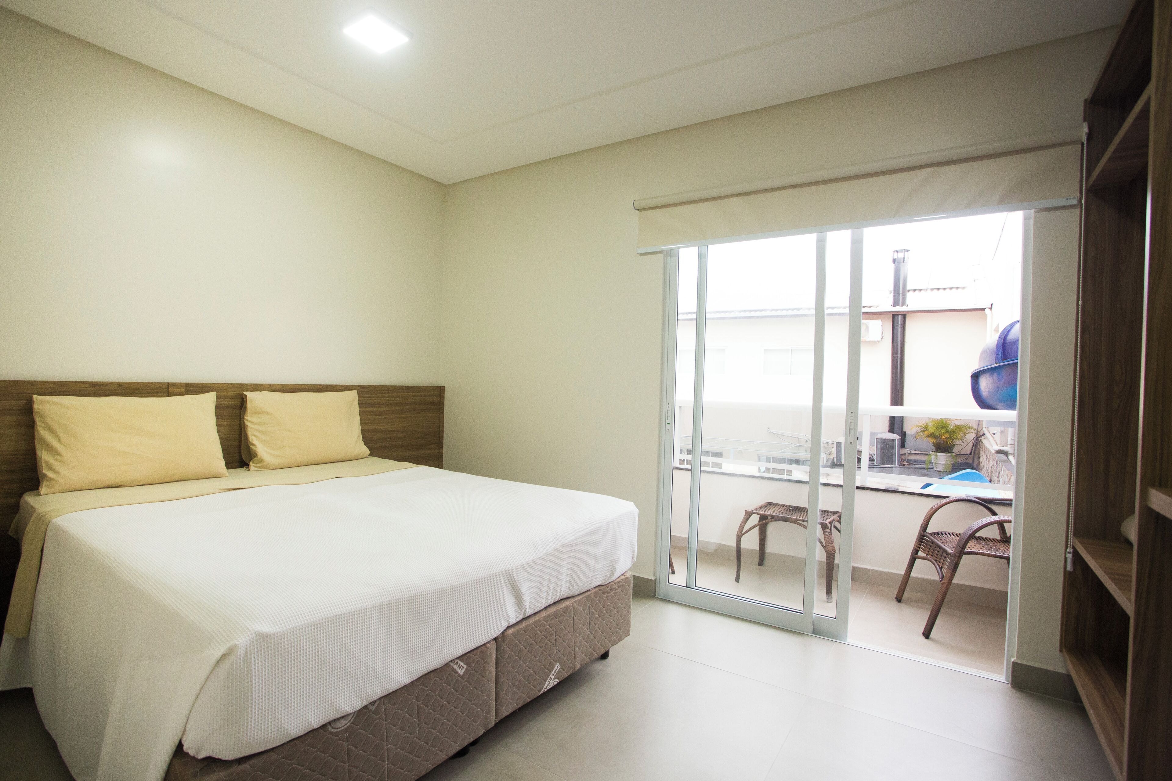 A bedroom with a bed, a sliding glass door leading to a balcony with chairs and a table.