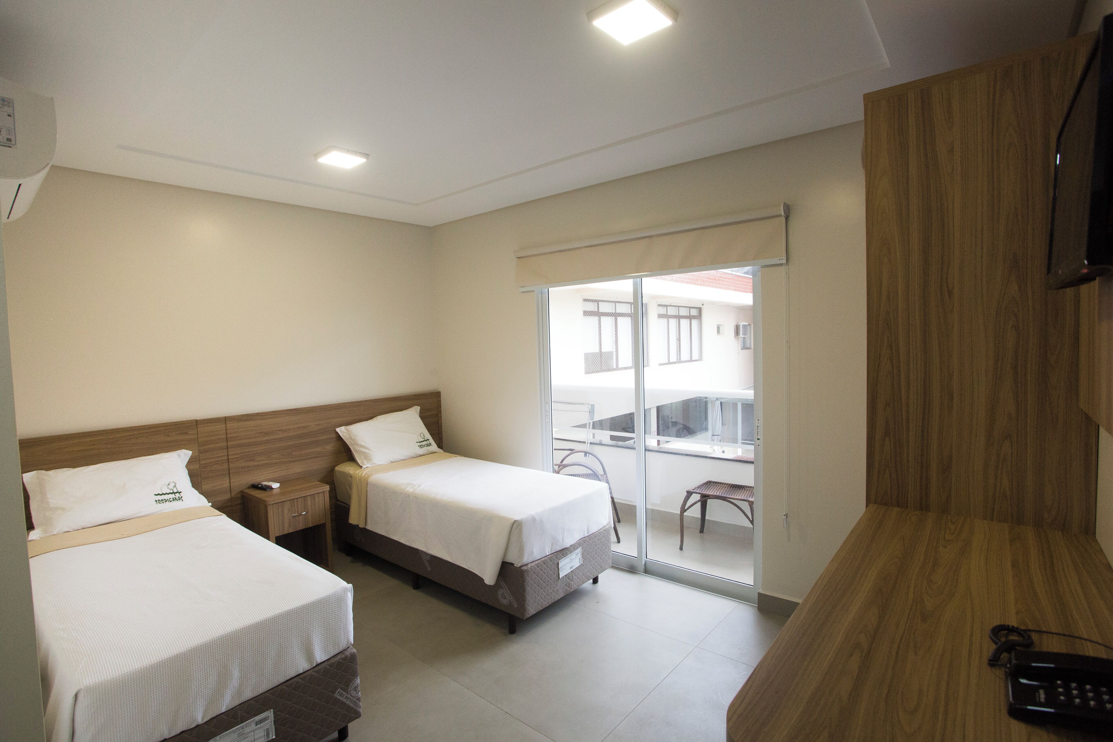 A hotel room with two beds, a wooden desk, a TV, and a balcony with a view.