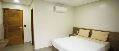 A bedroom with a bed, a wooden door, a wall-mounted air conditioner, and a bedside table.