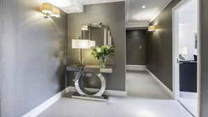 Un couloir moderne agrémenté d’un miroir, d’une table ronde avec une lampe et d’un vase rempli de fleurs.