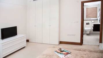 A room with a TV on a white cabinet, a magazine on the floor, and a wardrobe with a mirror.