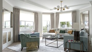 Un salon moderne avec un canapé, des fauteuils, une table basse et une vue sur la ville grâce à de grandes fenêtres.