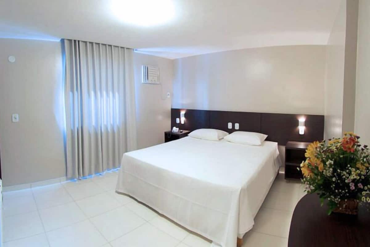 A hotel room with a large bed, a bedside table, a TV, and a flower arrangement.