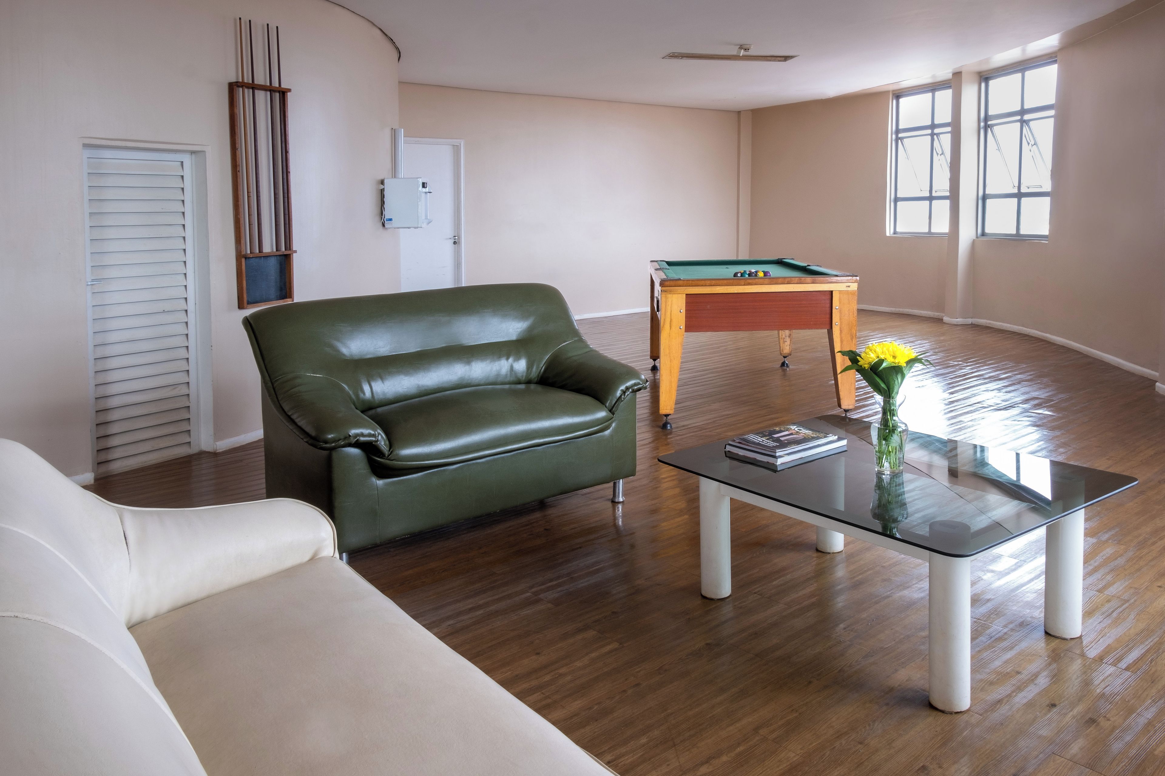 A living room with a green leather sofa, a glass coffee table, and a pool table.