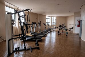 Une salle de sport spacieuse, équipée de divers appareils de musculation et de cardio, dotée de grandes fenêtres et d’un extincteur fixé au mur.