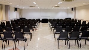 Une salle de conférence avec des rangées de chaises noires disposées face à un écran noir situé au fond de la salle.
