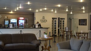 Un espace d’accueil d’hôtel avec un canapé marron, un canapé gris, un minibar et un panneau indiquant le « Tower Franca Hotel ».