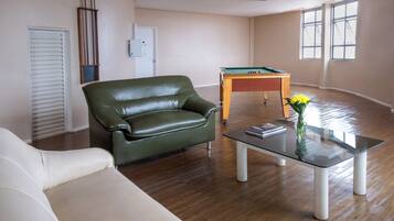 Una sala de estar con un sofá de cuero verde, una mesa de centro de vidrio y una mesa de billar.