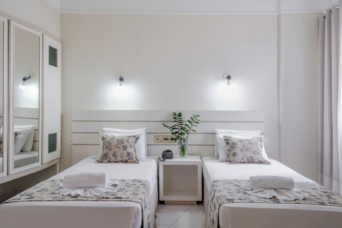 A hotel room with two beds, a nightstand with a phone, a mirror, and a plant.