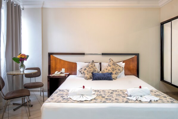 Una habitación de hotel con una cama bien hecha, una mesita con un florero y dos sillas.