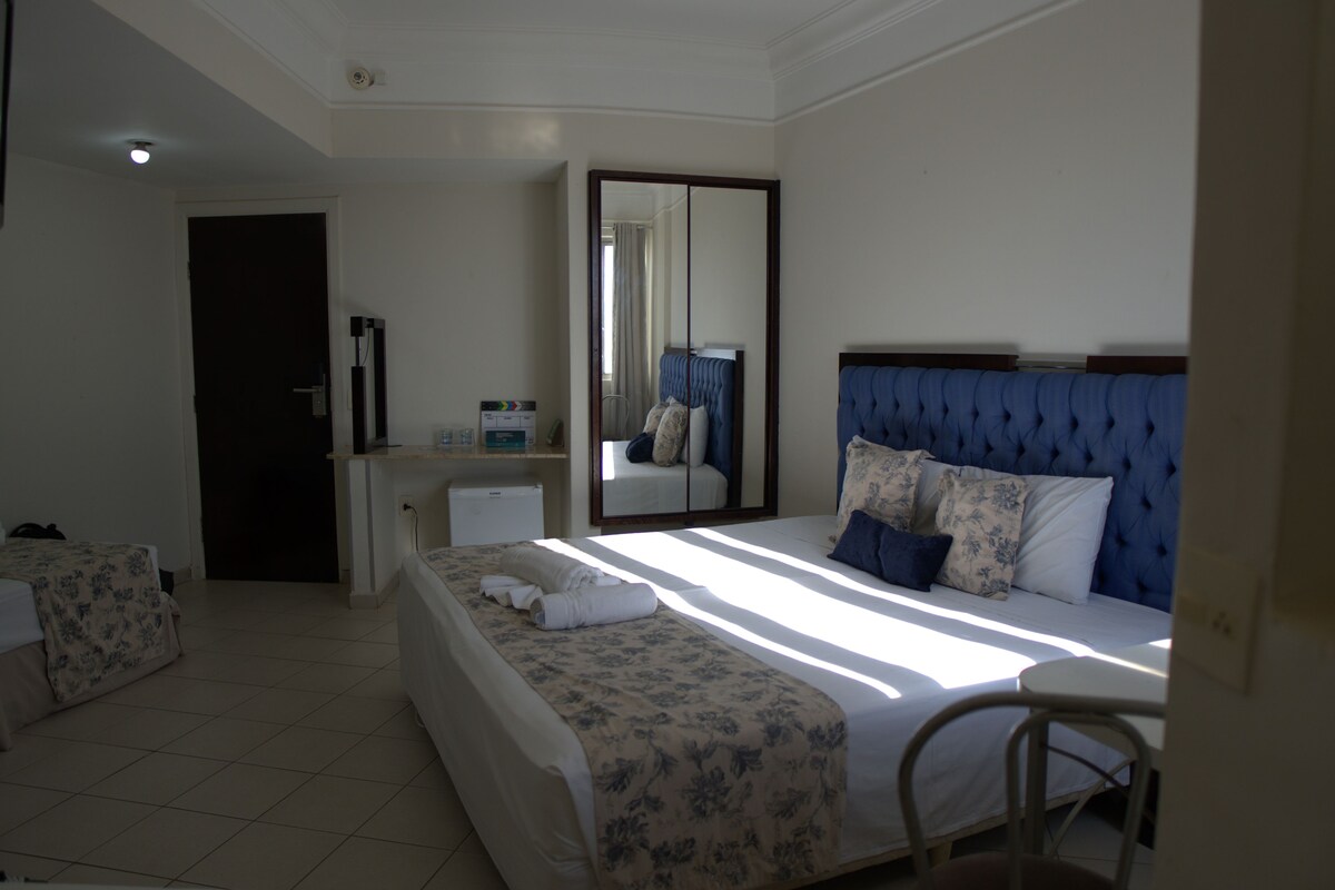 A hotel room with a large bed, a desk, a chair, and a mirror.