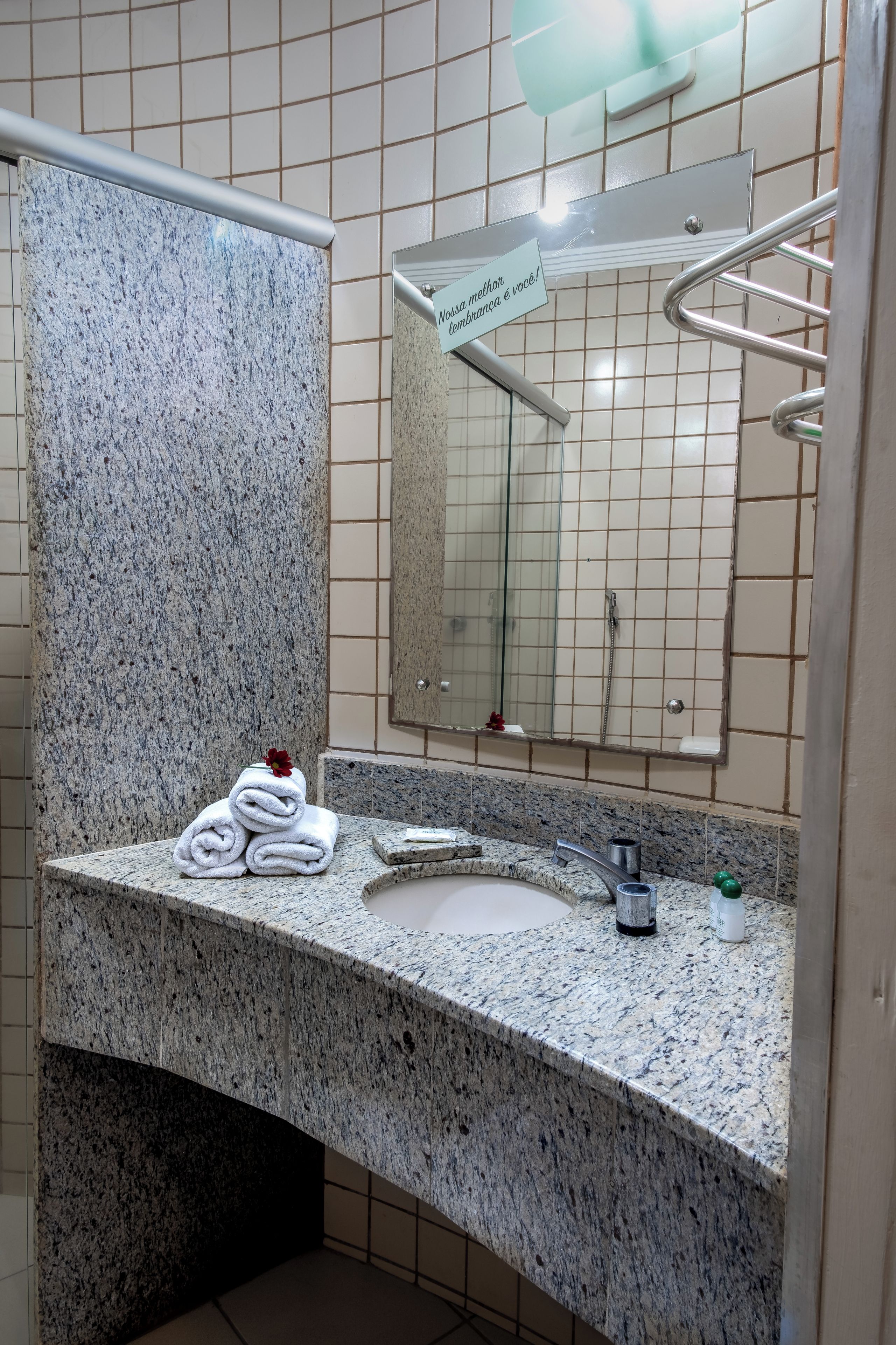 Un baño con encimera de granito, un lavabo, un espejo y un perchero para toallas.