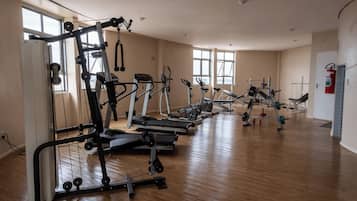 A spacious gym with various cardio and strength training equipment, large windows, and a fire extinguisher on the wall.