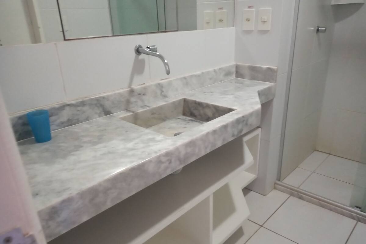 A bathroom with a marble sink, a blue trash bin, and a glass shower enclosure.