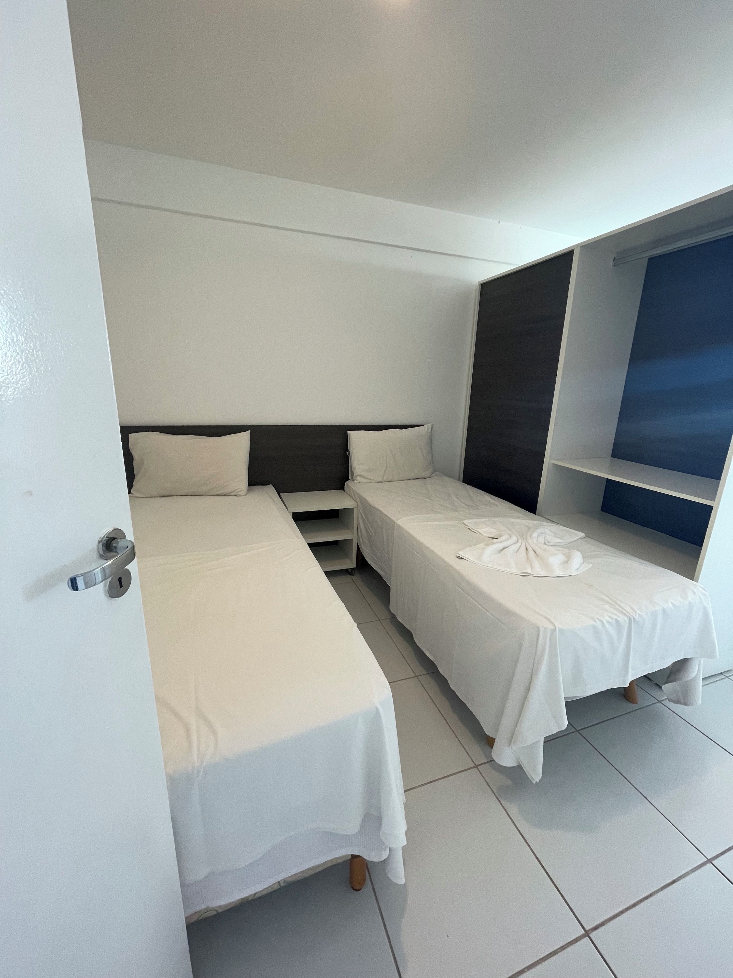 A hotel room with two single beds, a small table, and a window with a view.