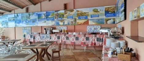 A restaurant with multiple tables and chairs, a buffet setup, and a wall decorated with regional maps.