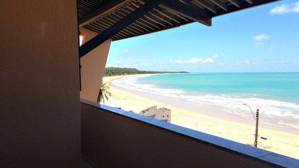 A beach view from a covered balcony with a view of the ocean and a sandy beach. - Atlântico Hotel (Maceió)