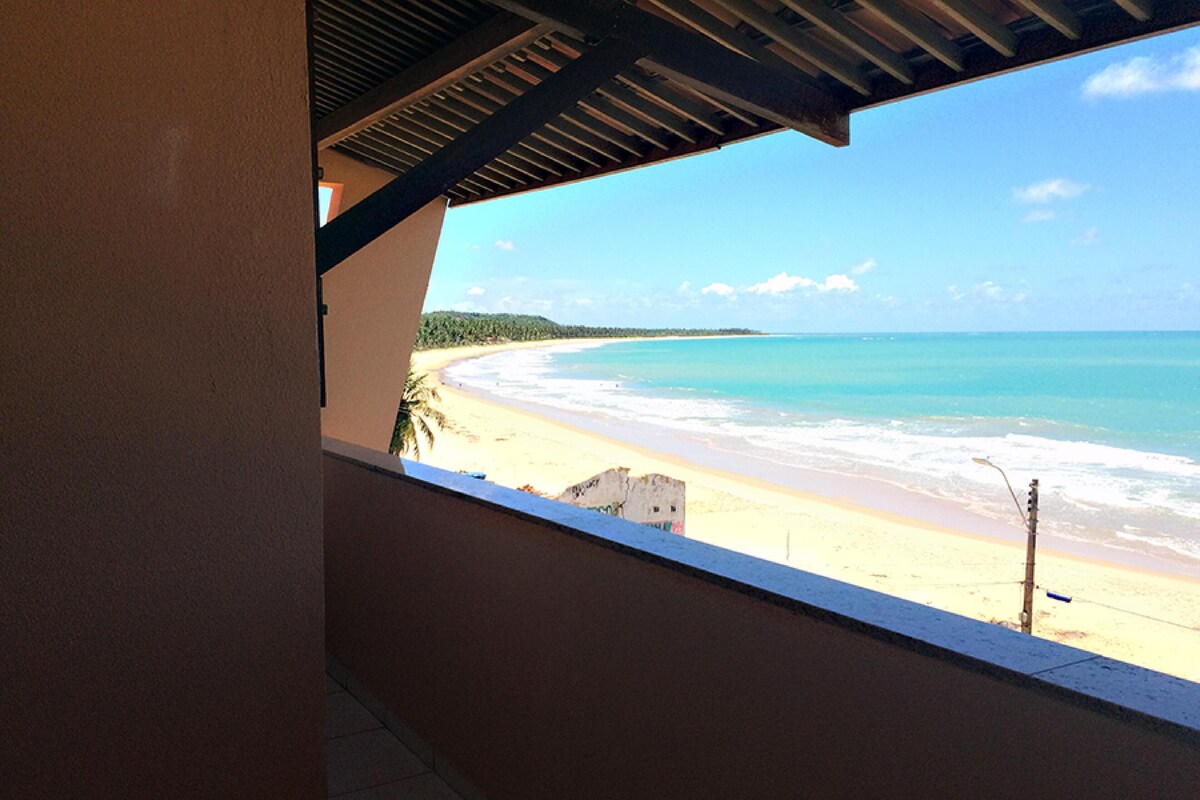 Une vue sur la plage depuis un balcon couvert, avec vue sur l’océan et une plage de sable.