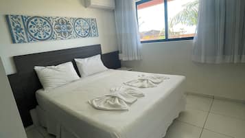 A hotel room with a bed, a window with curtains, a ceiling light, and a wall-mounted air conditioner.