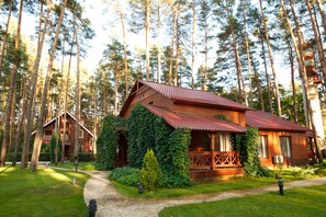 A wooden cabin with a red roof, surrounded by tall trees and a well-maintained lawn. - Grand Admiral Resort & SPA (Irpin)