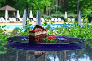 A dessert on a glass table with a pool and lounge chairs in the background. - Grand Admiral Resort & SPA (Irpin)