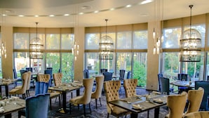 A restaurant with multiple tables and chairs, large windows with a view of greenery, and hanging chandeliers. - Grand Admiral Resort & SPA (Irpin)