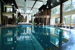A large indoor swimming pool with clear water, surrounded by lounge chairs and large windows. - Grand Admiral Resort & SPA (Irpin)