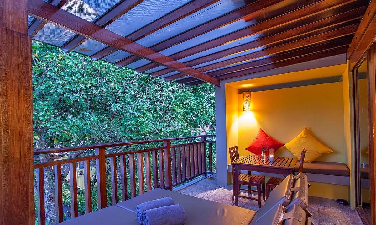 A balcony with a wooden railing, a table with chairs, a bench, and a lamp.