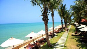 A beachside resort with sun loungers, umbrellas, and palm trees.