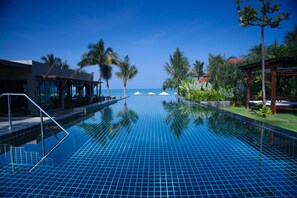 A clear blue infinity pool with a view of the ocean, surrounded by palm trees and a covered seating area. - Chongfah Resort (Takua Pa)