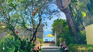 A pathway leading to a building with outdoor seating and a view of the sea.