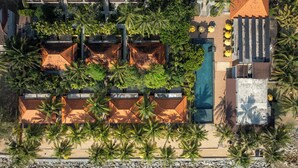 An aerial view of a resort with multiple bungalow-style accommodations, a swimming pool, and a beachfront.