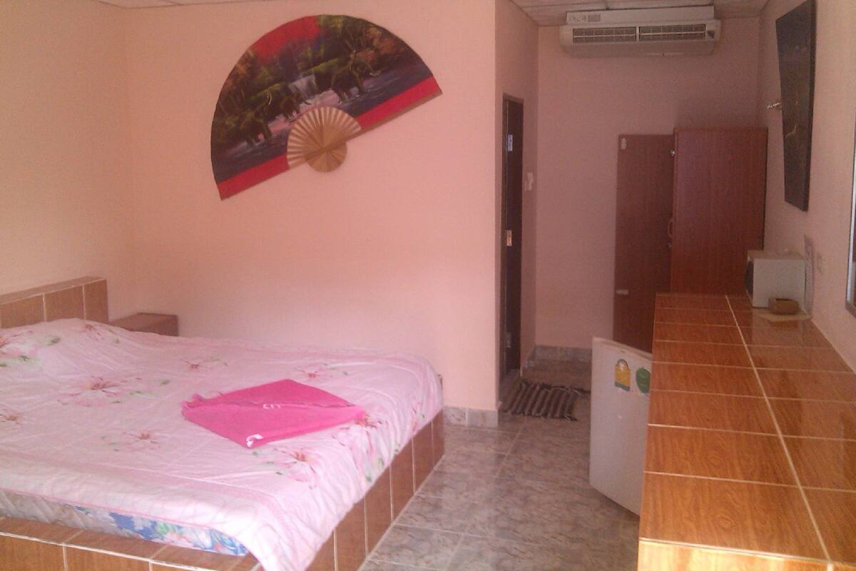 A bedroom with a bed, a fan, a door, and a tiled floor.
