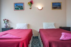 A room with two beds, each with a red bedspread and white pillows, a vase of flowers on a nightstand, and two framed pictures on the wall. - Klong Muang Inn (Krabi)